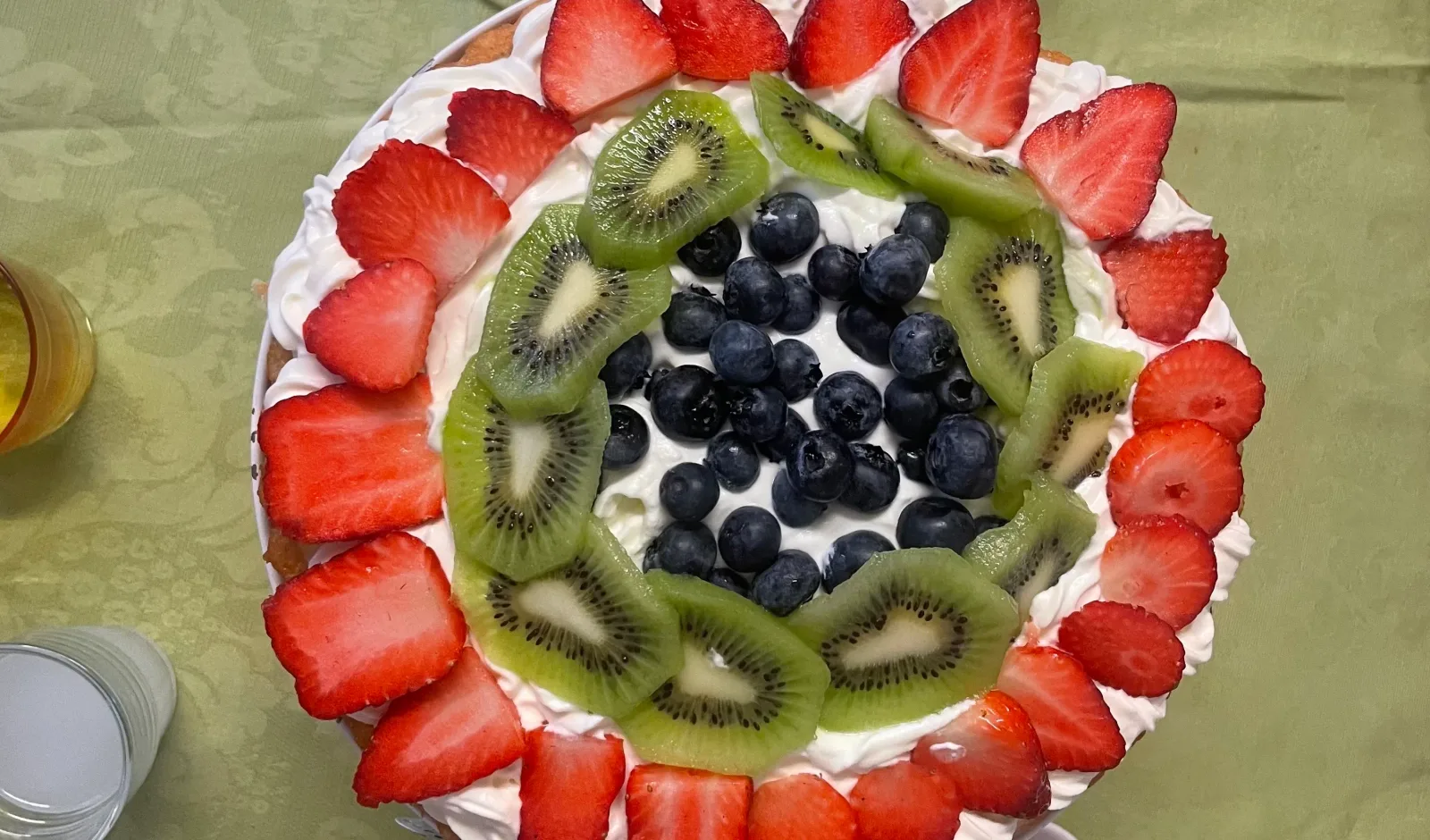Vegane Torte mit Kokoscreme, ringförmig belegt mit Erdbeerscheiben, Kiwischeiben und Blaubeeren in der Mitte